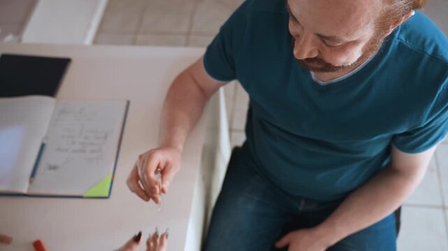 Man at kitchen table assessed by nurse, exchanging medication and notes, stethoscope on desk, overhead perspective, domestic interior, calm natural light, attentive caregiver providing guidance.