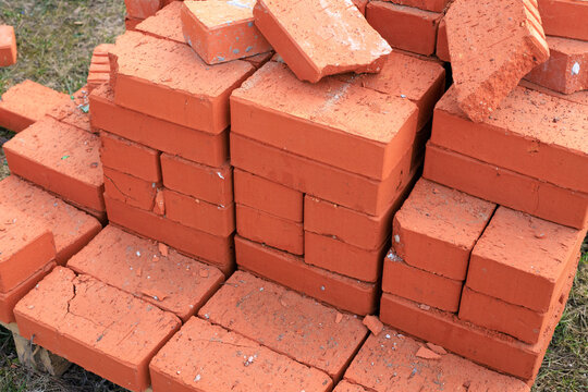 Red ceramic bricks stacked on a wooden pallet at a construction site. High-quality clay building blocks, ready for wall construction, home renovation