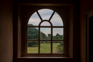 Fototapeta premium A symmetrical shot of a classic arched glass window looking out onto a wide green lawn. 