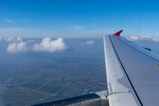 Aircraft wing with red winglet flying above clouds and fields