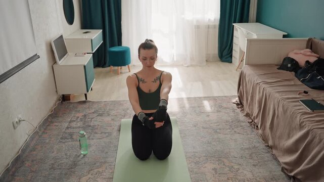 Indoor stretching routine for mobility. Female engaging in wrist and shoulder warmup exercises indoors. Woman performing focused mobility exercises on mats with water nearby in bedroom environment