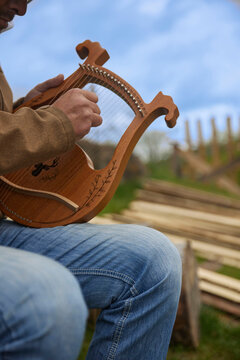 Man playing a wooden lyre harp outdoors.