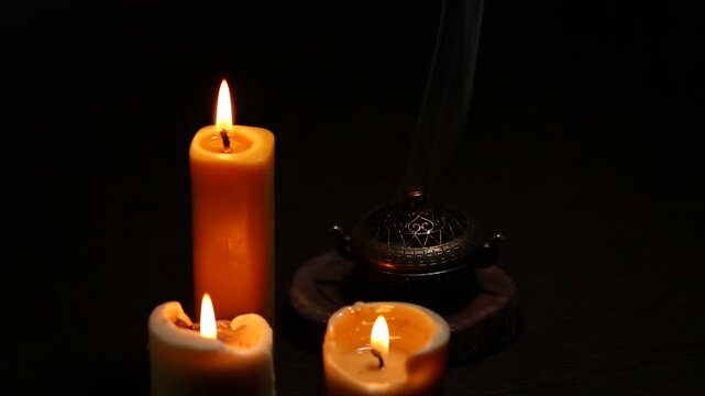 Three magic Christmas wax candle flames calm burning in home in white smoke from incense aroma stick on black dark background with copy space. Closeup yoga, spa, wellness, relaxation. No people