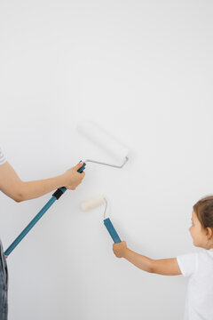 A parent and child are painting a white wall with rollers, engaging in a home improvement activity