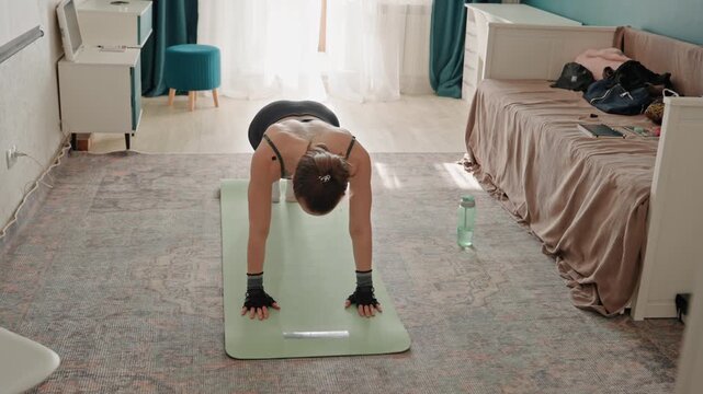 Home bedroom fitness white woman prepping for pushups on green mat, wearing fingerless gloves, water bottle at side, soft natural light, carpeted floor, focused breathing, beginner strength routine