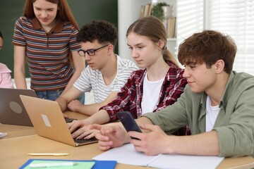 Group of students studying with laptops and notebooks at wooden desk in classroom © New Africa