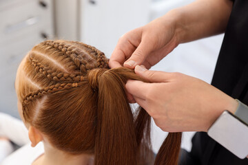 Fototapeta premium Hairstylist braiding teenage girl's hair in salon, closeup
