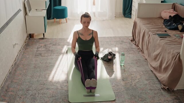 Woman performing full body resistance band routine on rug, centerframed mat near bed, steady cadence, online coach mode, athlete training vibe, core engagement, balance and conditioning focus