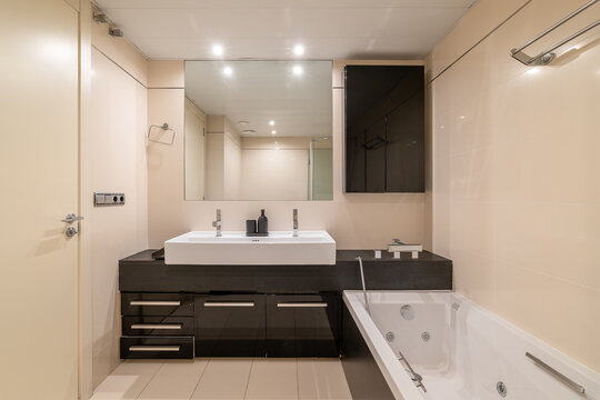 Modern bathroom with a sleek design. Features a large white sink, black cabinetry, a bathtub, and bright lighting. Clean and minimalist aesthetic.