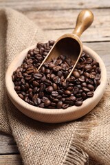 Fototapeta premium Coffee beans in bowl, scoop and burlap fabric on wooden table, closeup
