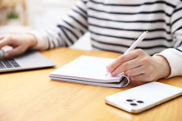 Fototapeta premium Woman taking notes while working with laptop at wooden table indoors, closeup