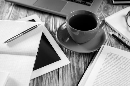 Modern cozy workspace setup with laptop, red coffee cup, open textbook and stationery on wooden background