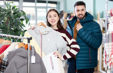 European woman choosing windbreaker next to man trying on down jacket in clothing store © JackF