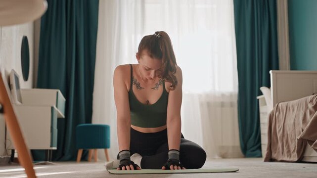 White woman seated core stretch home on mat, gentle pilates flow in sunlit bedroom with calm curtains and bedside table, instructor vibe focusing on breath, alignment and slow mobility for recovery