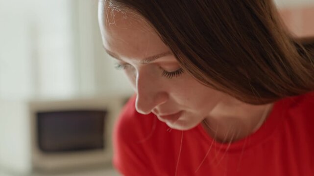 Thoughtful woman analyzing her workout schedule. Calm female reviewing fitness journal beneath gentle daylight. Contemplative woman studying her home exercise journal by soft natural window light