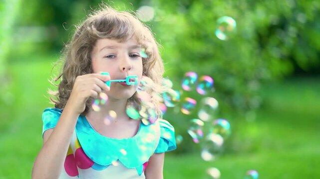 A happy child blows soap bubbles in a summer park. Slow motion