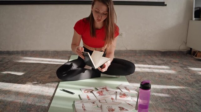 Individual preparing for exercise session at home. Lady arranging fitness cards and journal pages on carpet. Woman setting up her exercise routine with cards and journal in cozy home space