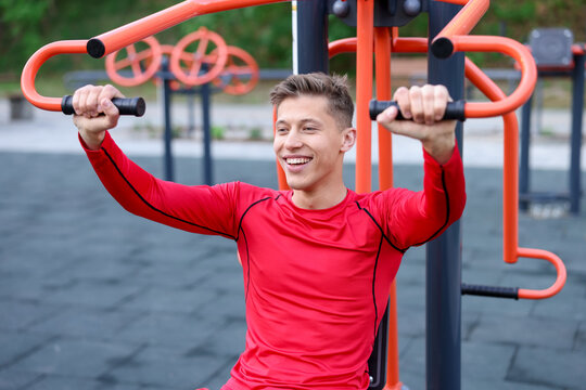 Athletic young man exercising on chest press machine at outdoor gym
