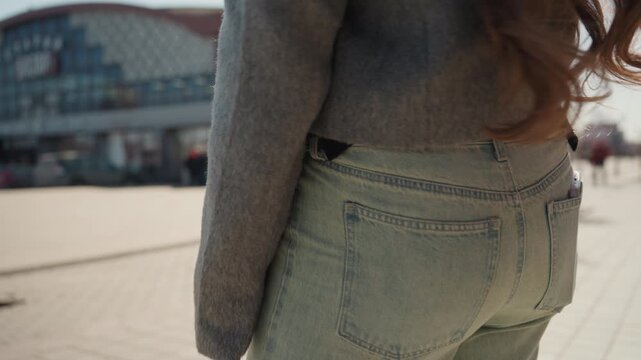 Casual city fashion snapshot. Young woman features casual denim look with tech gadgets outdoors. Modern urban woman highlights her denim fashion style with mobile in natural sunlight