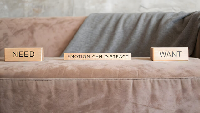 Need vs Want: Wooden blocks with 'Need', 'Emotion Can Distract', and 'Want' are placed on a textured sofa.