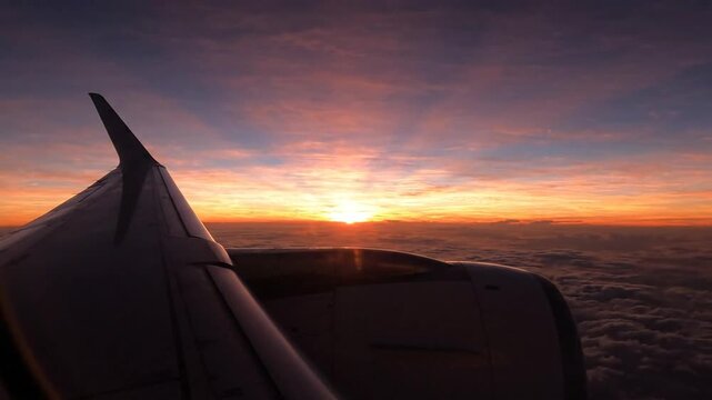 Airplane wing and sunrise over clouds during flight, aerial view