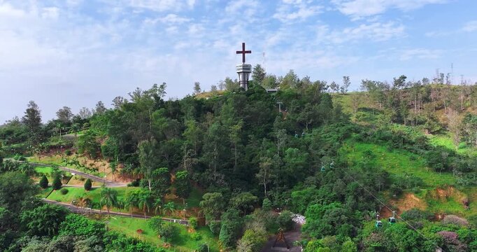 4K drone view of Morro do Cruzeiro in Aparecida, Brazil, featuring the iconic cross, cable cars and lush green landscape.