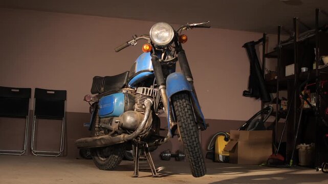 Old blue vintage motorcycle parked in a cluttered garage, awaiting restoration or repair a neglected classic project bike surrounded by tools, parts, and dusty workshop clutter
