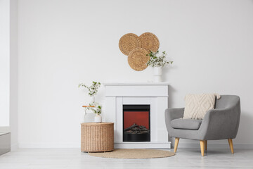 Obraz premium Interior of light living room with blooming branches in vases, fireplace and armchair