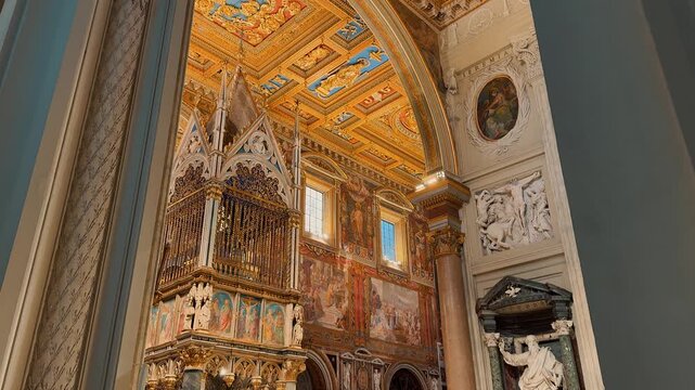 An incredible grand interior view showing the ornate golden ceiling, majestic marble columns, and exquisite religious artwork inside the historic Archbasilica of Saint John Lateran in Rome, Italy.

