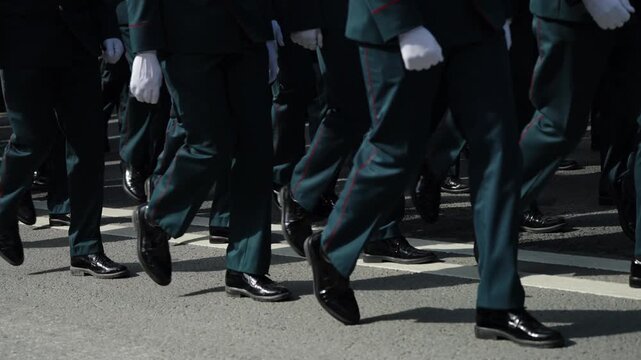 Close-up view of uniformed soldiers marching in tight formation, polished black shoes and white gloves moving in synchronized steps along a marked street during a ceremonial parade
