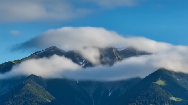 Serene vista of towering alpine peaks partially concealed by ethereal white clouds, creating a dramatic and tranquil natural landscape under a clear blue sky