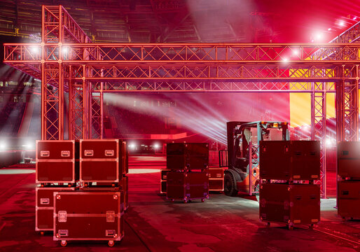 Event production setup. Forklift transports stage equipment cases beside concert truss structure with red performance lighting