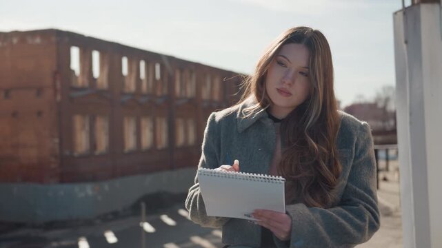 Contemplative diary by historic building. Thoughtful writer engaged in jotting notes amidst wind and history. Poignant scene of writer recording reflections on rooftop near ancient bricks