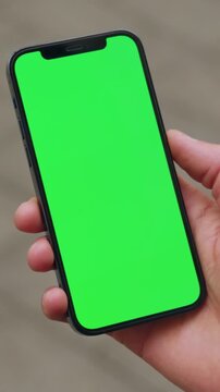 Person checks notifications casually outside, Close examination of hand holding smartphone with green screen outdoors