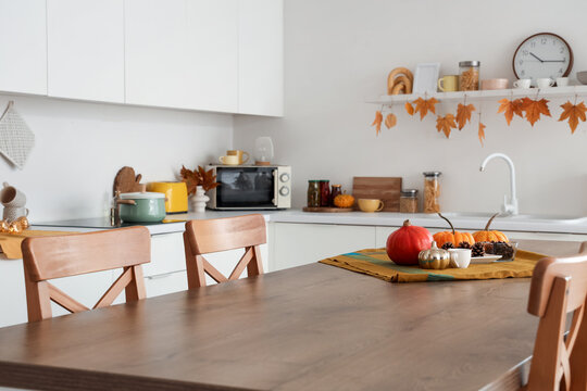 Wooden dining table with autumn pumpkins and pine cones in modern kitchen