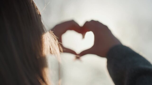 Pretty white woman holding heart with hands, backlit sunburst through bare branches, warm glow and vintage film grain, close framing, quiet gratitude, poet composing verse in winter light