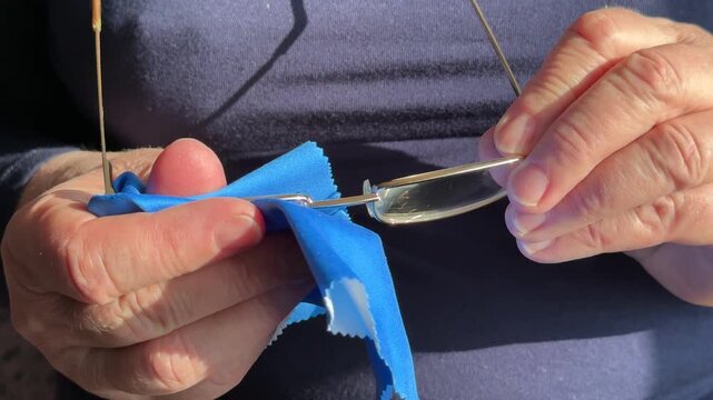 Closeup woman cleaning eyeglasses with blue microfiber cloth, sunlight catching gold frames and hands, slow deliberate wiping