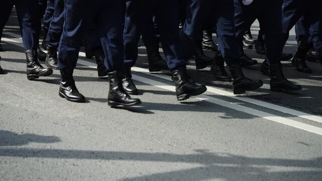 Close-up view of uniformed personnel marching in synchronized formation on a city street, black combat boots and navy trousers stepping in unison during a disciplined parade