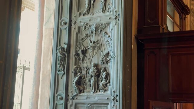 A crowd of tourists gather at the main gates inside the Basilica of Saint Mary Major, looking out towards the Piazza di Santa Maria Maggiore in Rome, Italy.

