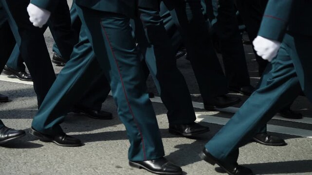 Close-up view of uniformed personnel marching in synchronized formation during a formal parade, polished black shoes and dark trousers stepping in unison along asphalt roadway