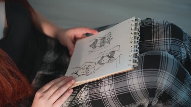Caucasian woman holding sketchbook with prophecy sketches, closeup of redhead hands flipping spiral pages on plaid skirt, soft natural light and intimate mood, amateur fortuneteller studying symbolic