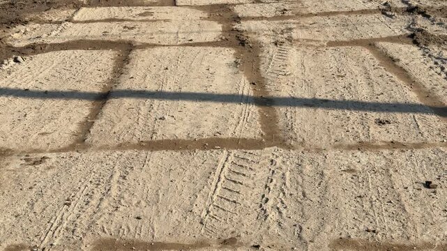 Temporary concrete slab road covered mud, sunlit construction corridor with deep tire tracks, sand packed joints between slabs