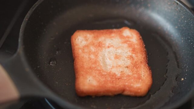 Skillet frying square luncheon meat, golden crust forming while oil bubbles and sizzle intensifies closeup view shows crisp texture and warm brown tones, morning comfort scene suggesting simple