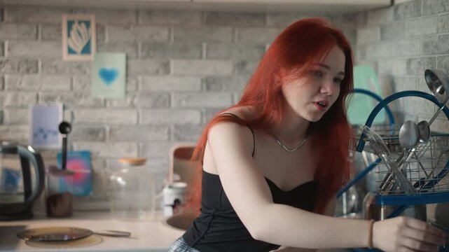 Red haired woman reaching across counter, modern brick backsplash kitchen, casual black top, handling pastry while pondering next move, soft window light, domestic stillness, subtle foresight