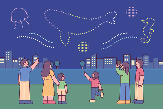 Family watching a colorful drone light show above a city skyline at night, featuring marine shapes and outdoor festival atmosphere.