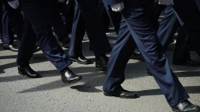 Close-up of uniformed marchers moving in precise formation along an asphalt street, polished black shoes and white gloves visible as they step in sync during a ceremonial parade