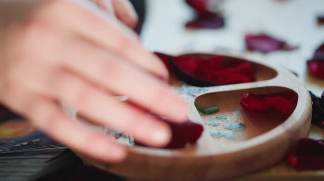 Hands sorting rose petals into dish, fingers placing petals in wooden compartments, closeup of tactile ritual and salt crystals, reader counting and arranging for fortune practice, gentle movement
