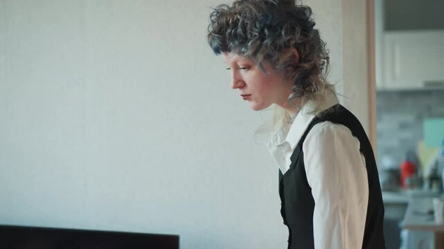 Curly woman prepares red candle near doorway then arranges ritual setup on bed, careful hands strike match, smoke rises from wick, focused expression, small kitchen in background, cozy apartment mood,