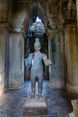Fototapeta premium A stone statue of a deity stands within the ancient ruins of Angkor Wat, Siem Reap, Cambodia. The temple complex is a UNESCO World Heritage site.
