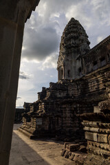 Fototapeta premium Angkor Wat temple complex in Siem Reap, Cambodia, at sunset. The ancient Khmer architecture is bathed in dramatic light and shadow under a cloudy sky.